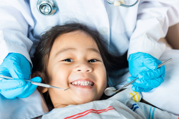 Paediatric dentistry Dental kid health examination. Doctor examines oral cavity of little child uses mouth mirror to checking teeth cavity, Asian dentist making examination procedure for smiling cute little girl